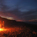 Some people around a fire at the beach.